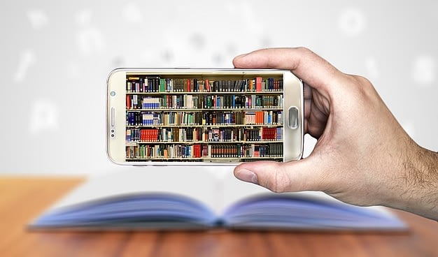 A hand holding a mobile phone with a book in the background