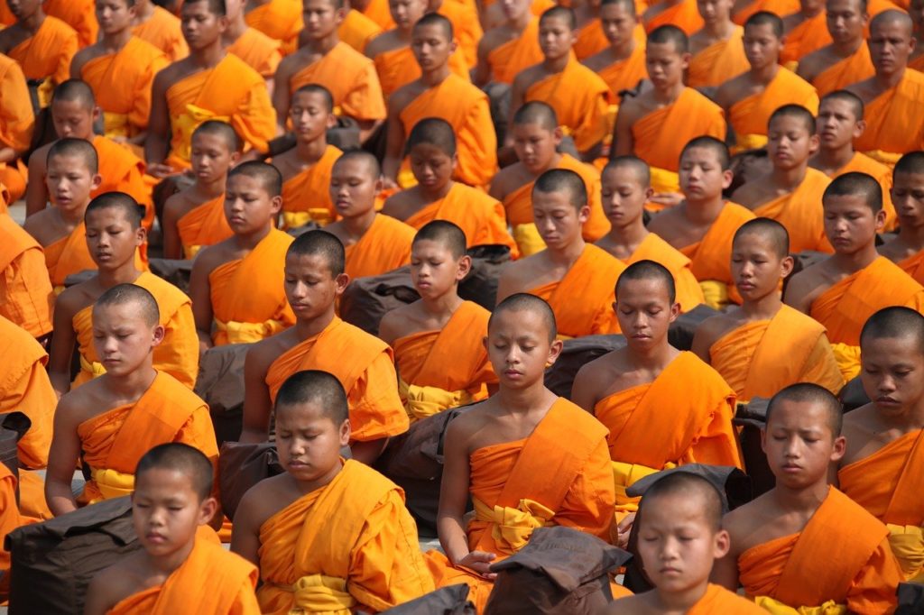 Must watch videos religion. Image of young Buddhist men in orange robes sitting in rows with eyes closed.