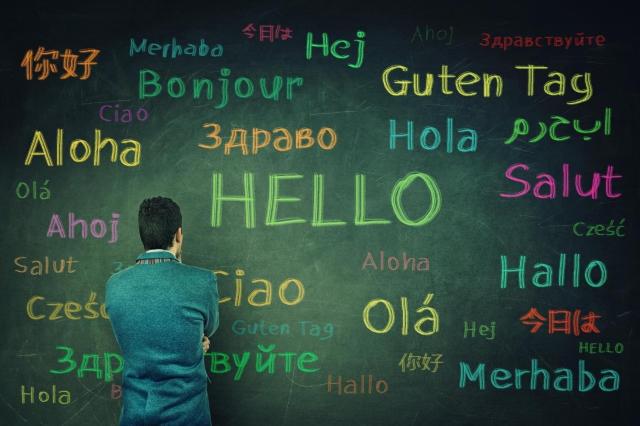 Language structure phonology morphology syntax: Image of a man standing next to a chalkboard with hello written in different languages.