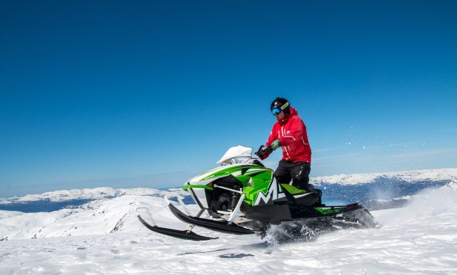 A man riding a snowmobile in the snow on a bright sunny day.